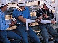 Behind the chutes, saddle bronc riders tape up for a ride in which the taped arm is keeping the cowboy on the bronc. photo by Hillary Mayberry